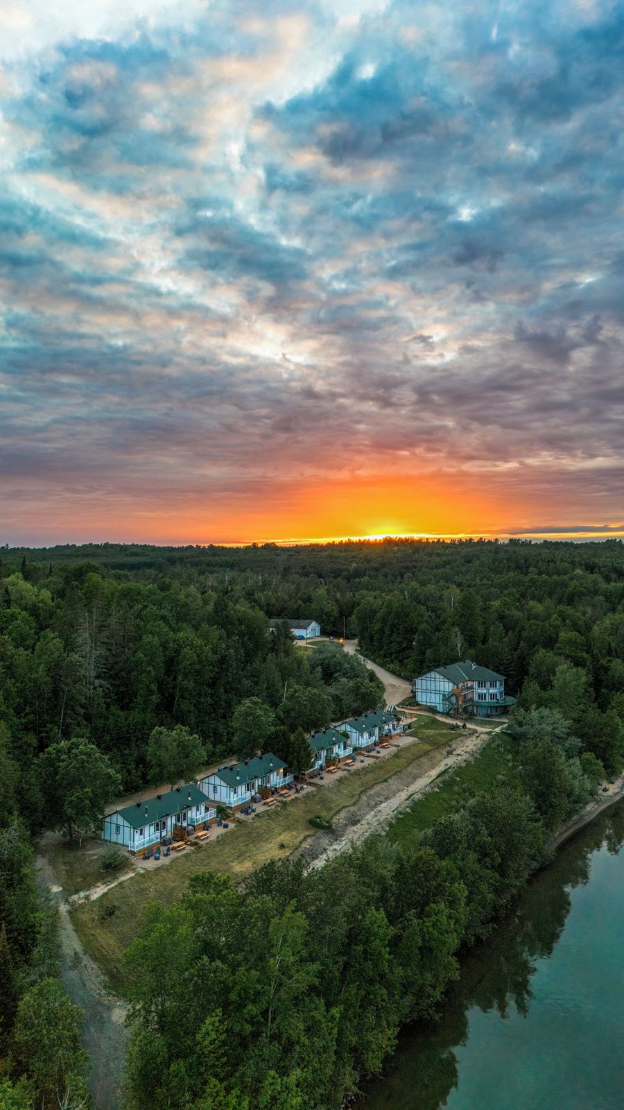 Een vakantieverblijf aan het meer met meerdere chalets, een steiger en een bebost landschap.