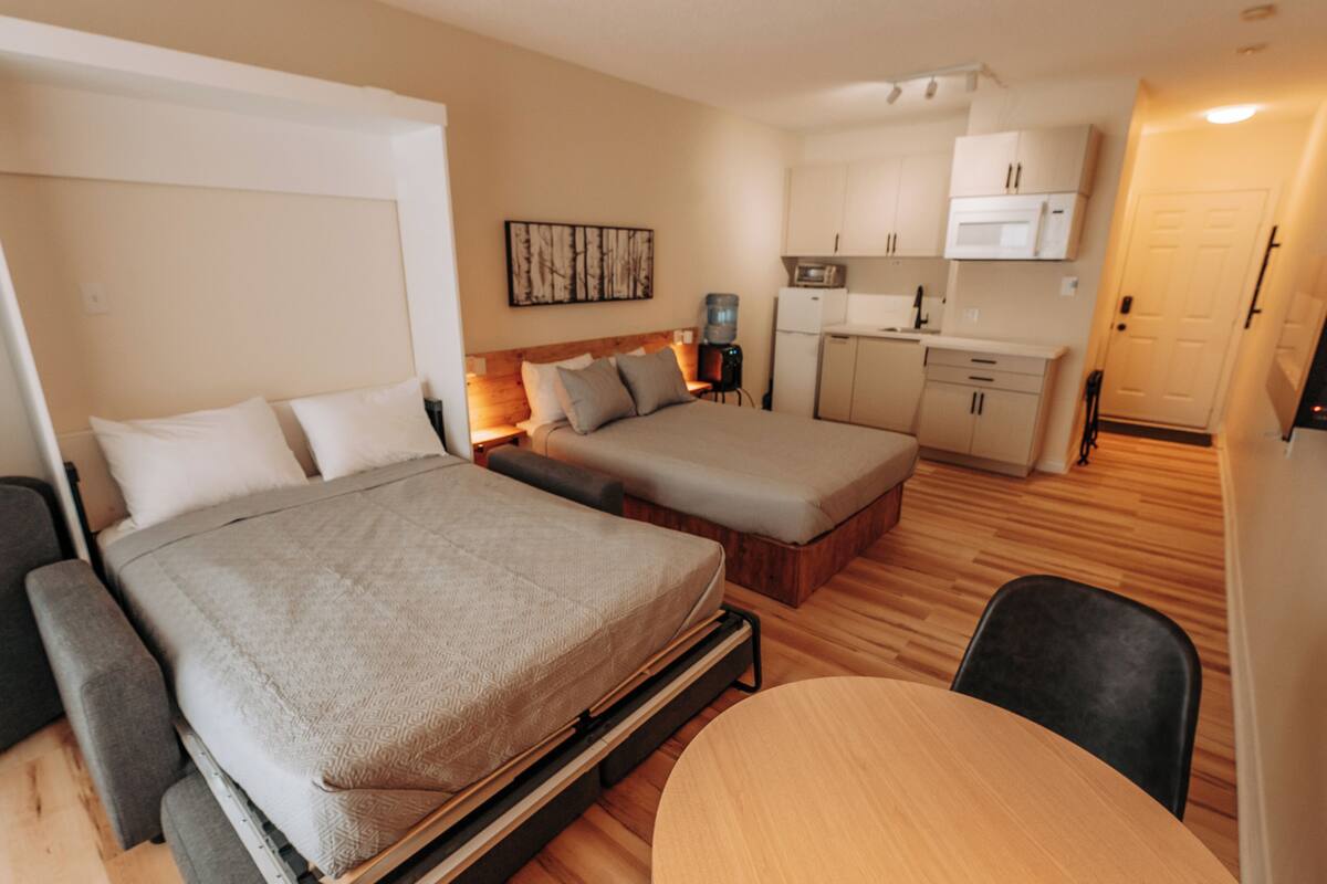 Ein kleines Hotelzimmer mit Bett, einer kleinen Sitzecke, einem Esstisch und einer Küchenzeile.