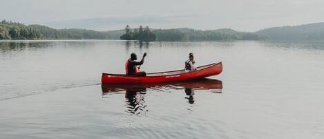 A red canoe on calm water with two people, surrounded by a forested landscape.