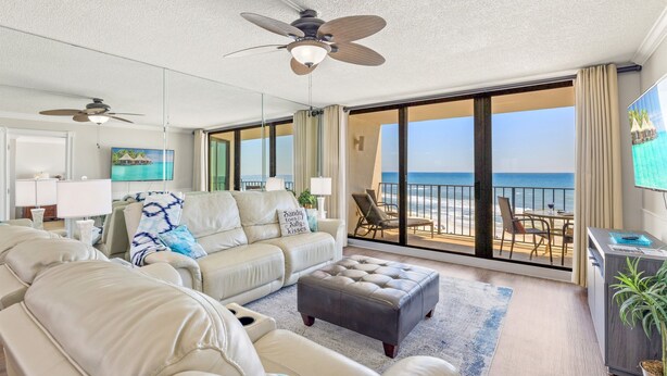 A spacious living room with a large sofa, a coffee table, and a balcony with a view of the ocean.