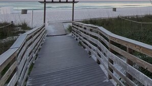 A wooden boardwalk leading to a beach with a wooden pergola structure.