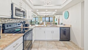 A modern kitchen with white cabinets, a stainless steel oven, a dishwasher, and a large window offering a view.