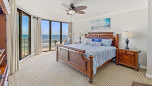 A bedroom with a large bed, a nightstand, a ceiling fan, and a view of the ocean.