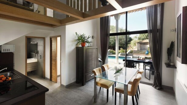 A modern kitchen with a glass dining table and chairs, a built-in oven, and a view of the backyard. - Villa Bonifacio Les Maquisardes (Bonifacio)
