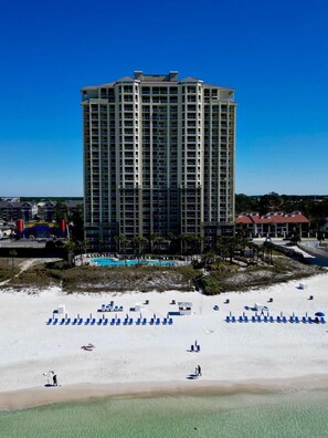 Hotel alto com várias varandas, piscina e área de praia com espreguiçadeiras.
