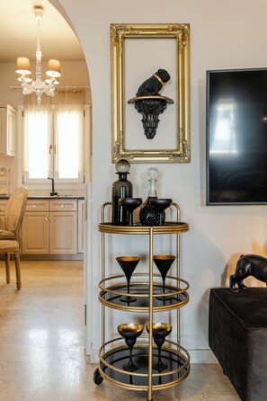 Ein mehrstufiger schwarzer und goldener Tisch mit Gläsern, einem gerahmten Kunstwerk und einem Fernseher an der Wand.
