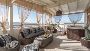 Un espace extérieur lumineux, aménagé avec un canapé, deux poufs à motifs, une table basse en verre, un jacuzzi et un cactus.