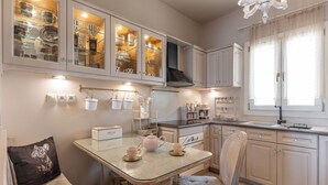 Une cuisine avec des meubles blancs, une table à plateau en verre et un fauteuil suspendu.