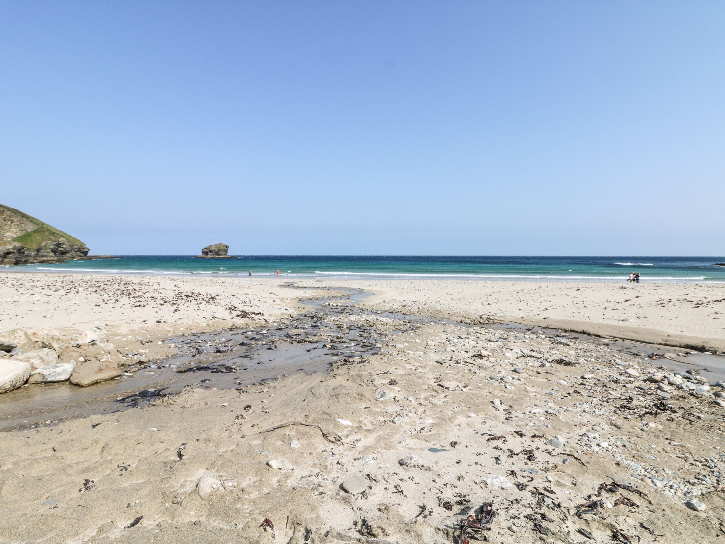 A beach with a rocky foreground, a clear sky, and calm sea.