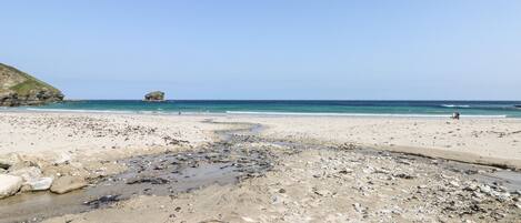 A beach with a rocky foreground, a clear sky, and calm sea.