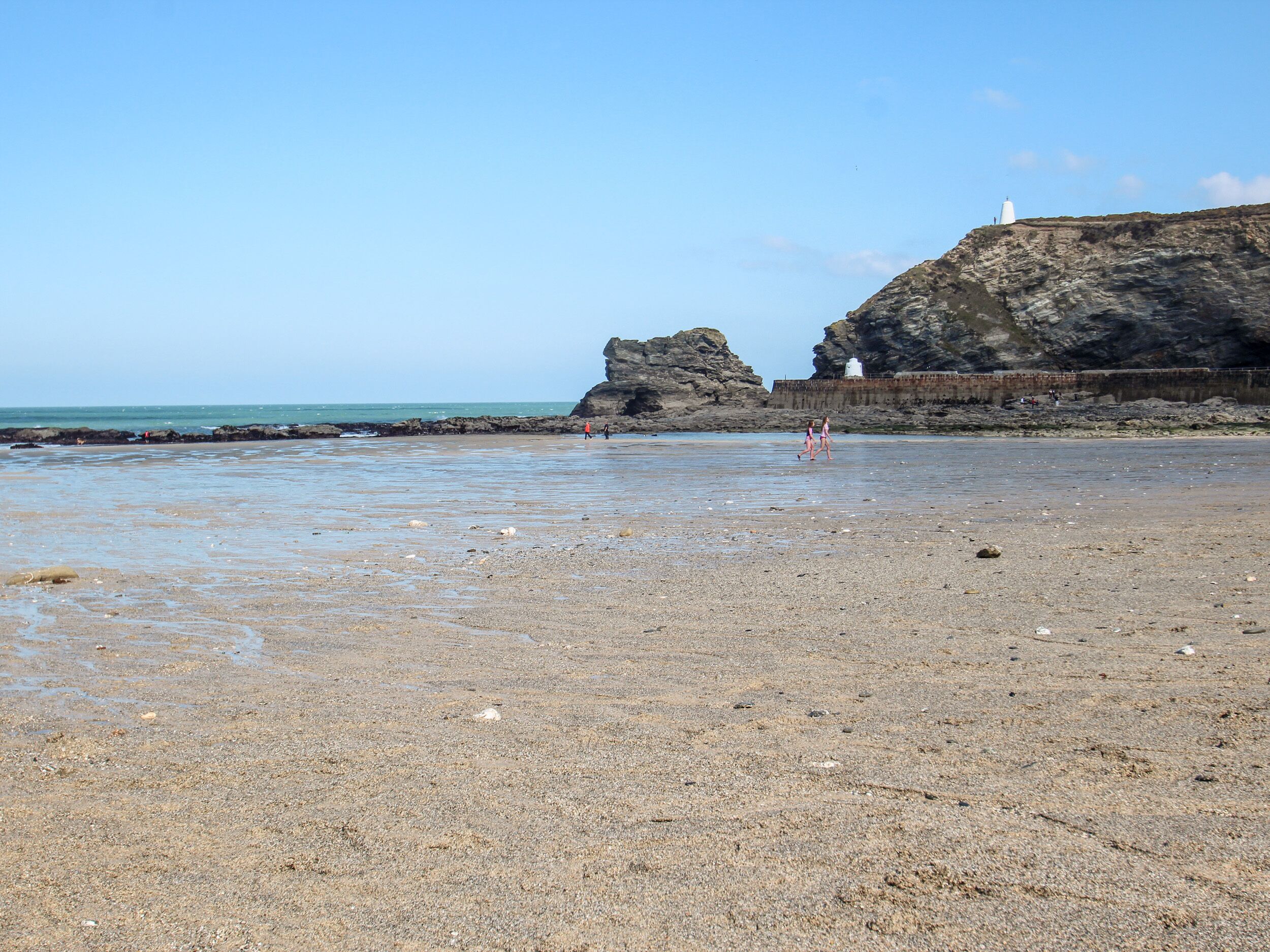 A rocky beach with a lighthouse and a rocky cliff in the background.