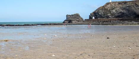 A rocky beach with a lighthouse and a rocky cliff in the background.