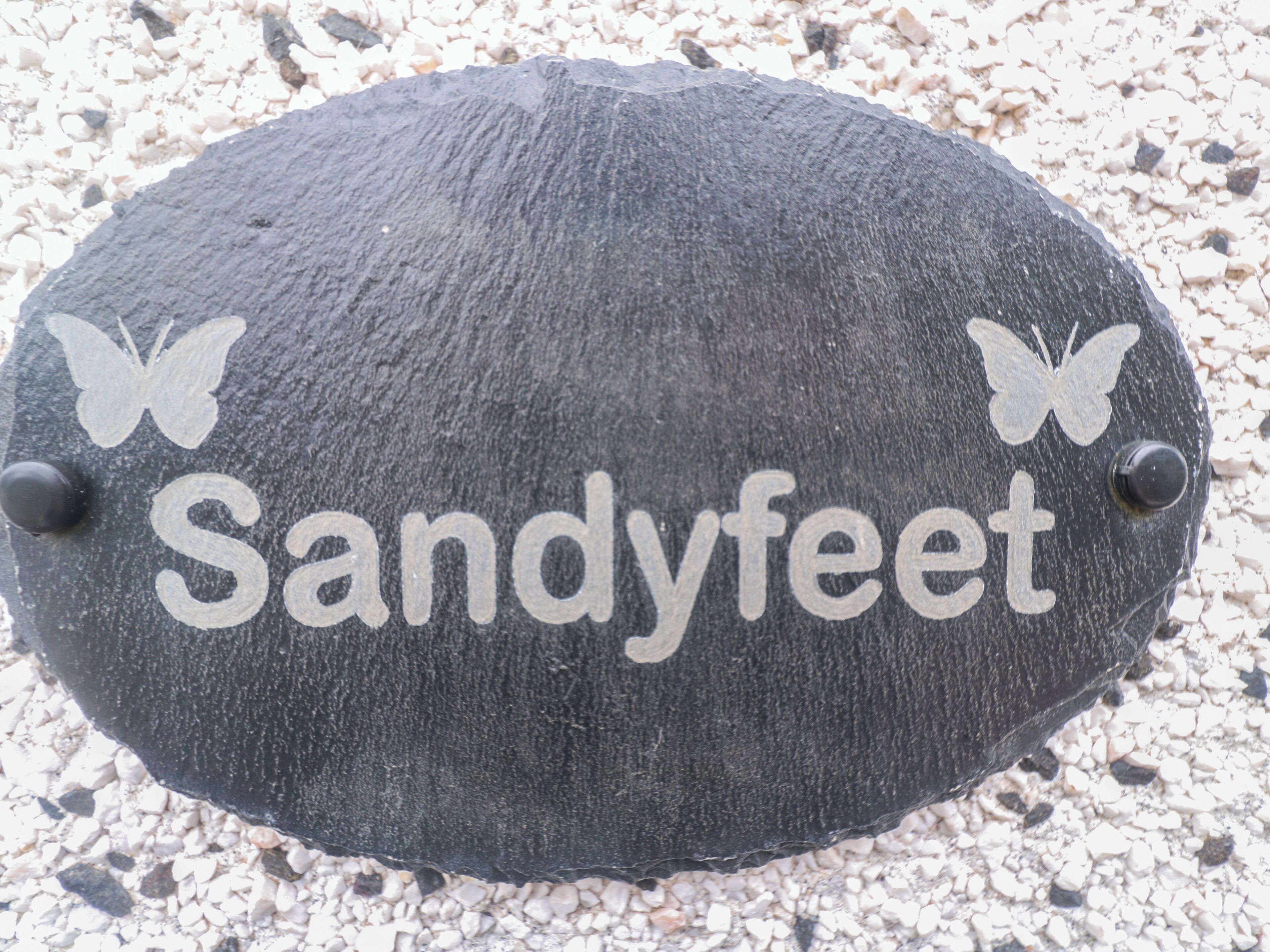 A slate sign with 'Sandyfeet' and butterfly decorations.