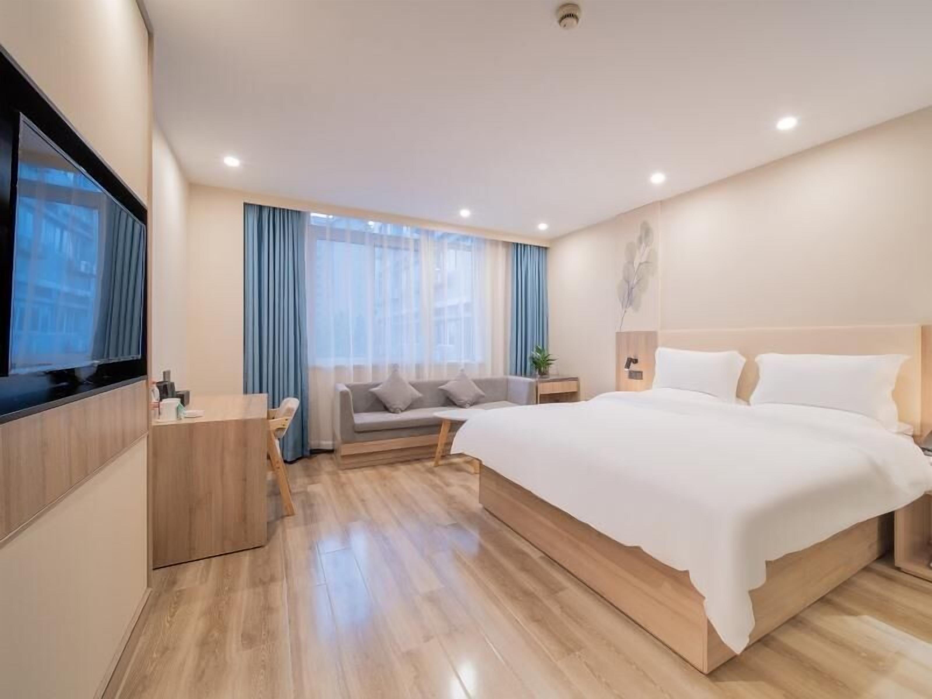 A modern hotel room with a large bed, a TV, a desk, and a sofa.