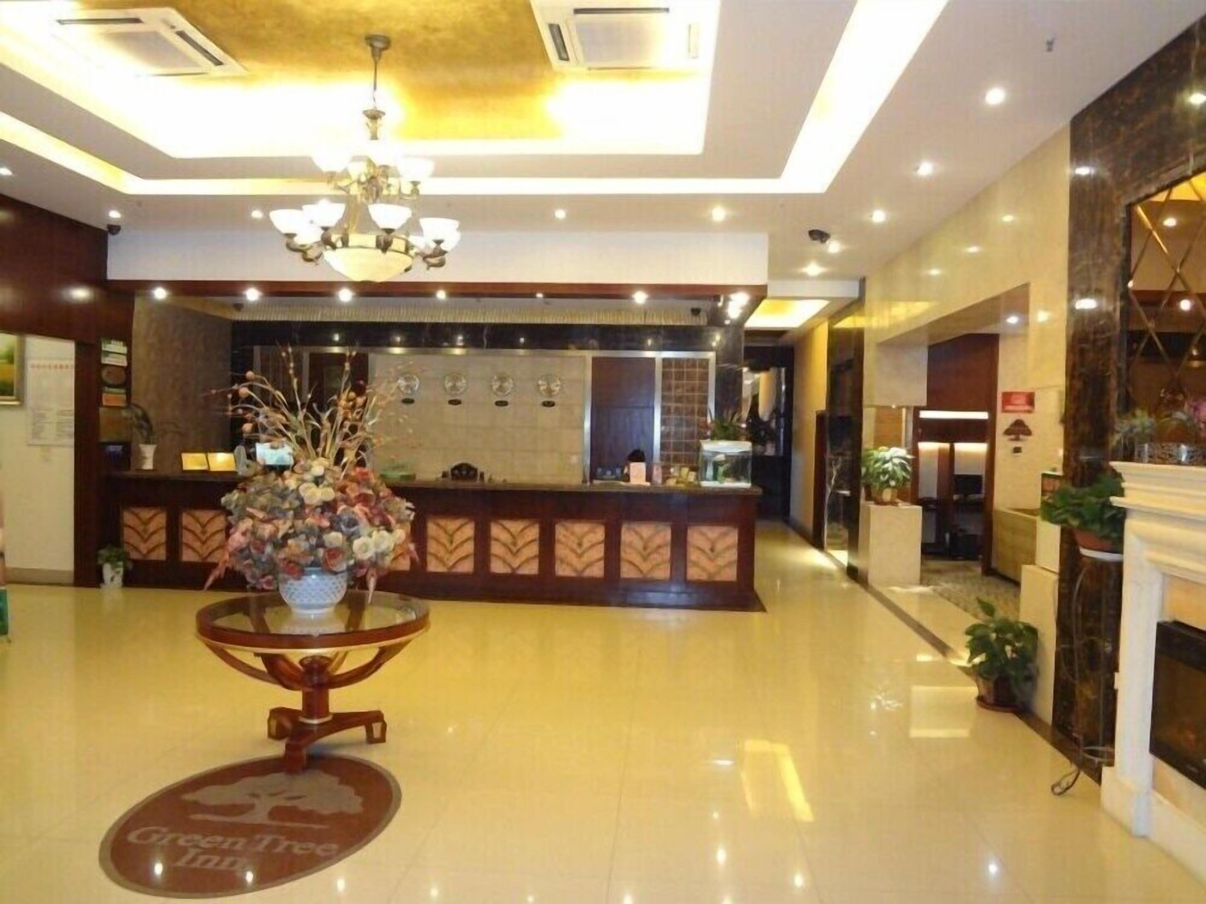 A hotel lobby with a reception desk, a chandelier, and a coffee table with a floral arrangement.