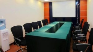 A conference room with a long table, black chairs, a projector screen, and a water dispenser. - Greentree Inn Nantong Jiaoyu Road Hotel (Nantong)
