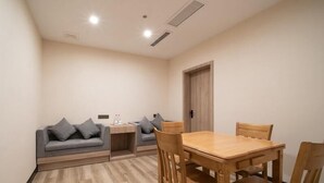 A room with a wooden dining table and four chairs, a grey sofa with cushions, a small side table, and a door with a wooden frame. - Greentree Inn Nantong Jiaoyu Road Hotel (Nantong)