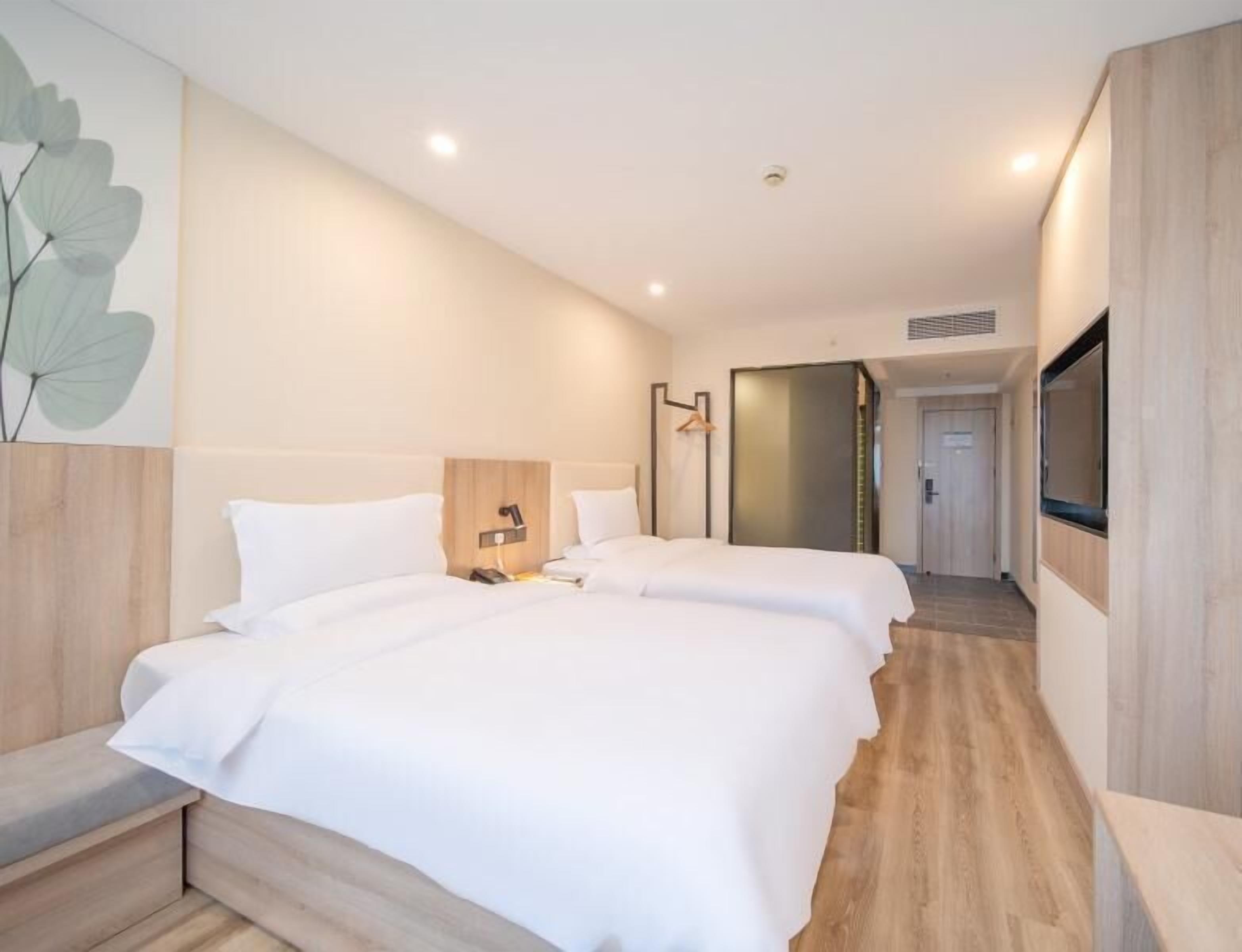 A modern hotel room with two beds, a wooden headboard, a bedside table, a wall-mounted TV, and a large window.