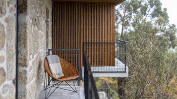 Pared exterior de piedra, una silla de mimbre con una manta y barandilla de balcón de listones de madera.