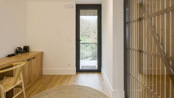 Une chambre moderne avec un bureau en bois, une chaise, un petit tapis et une vue sur un balcon extérieur, accessible par une porte.