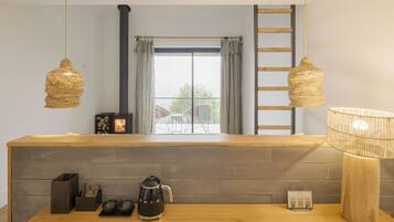 Una cocina moderna con encimera de madera, luminarias tejidas colgantes, una cafetera y vistas al exterior a través de un amplio ventanal.