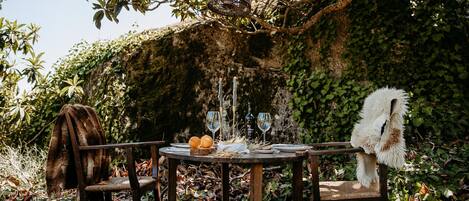 An outdoor dining setup with a rustic wooden table, two chairs, and a hanging light fixture.
