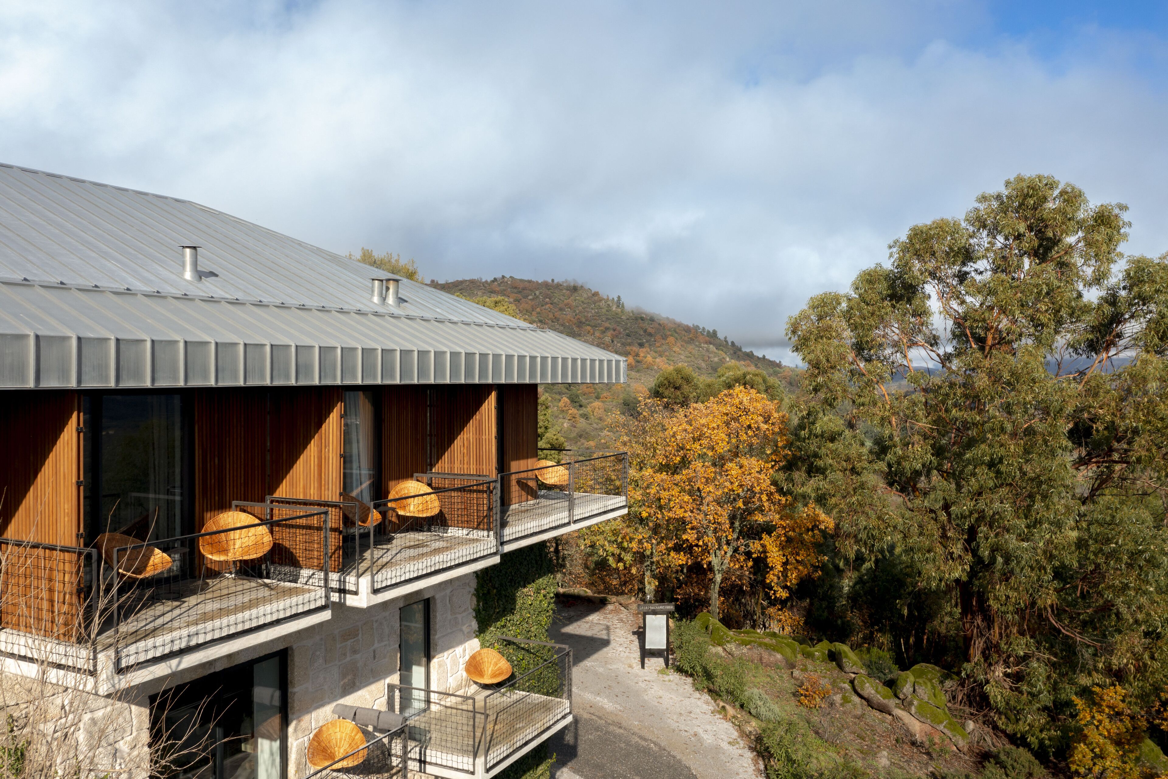 A modern house with a stone facade, wooden balconies, and a view of a forested hillside.