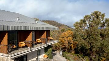 A modern house with a stone facade, wooden balconies, and a view of a forested hillside.
