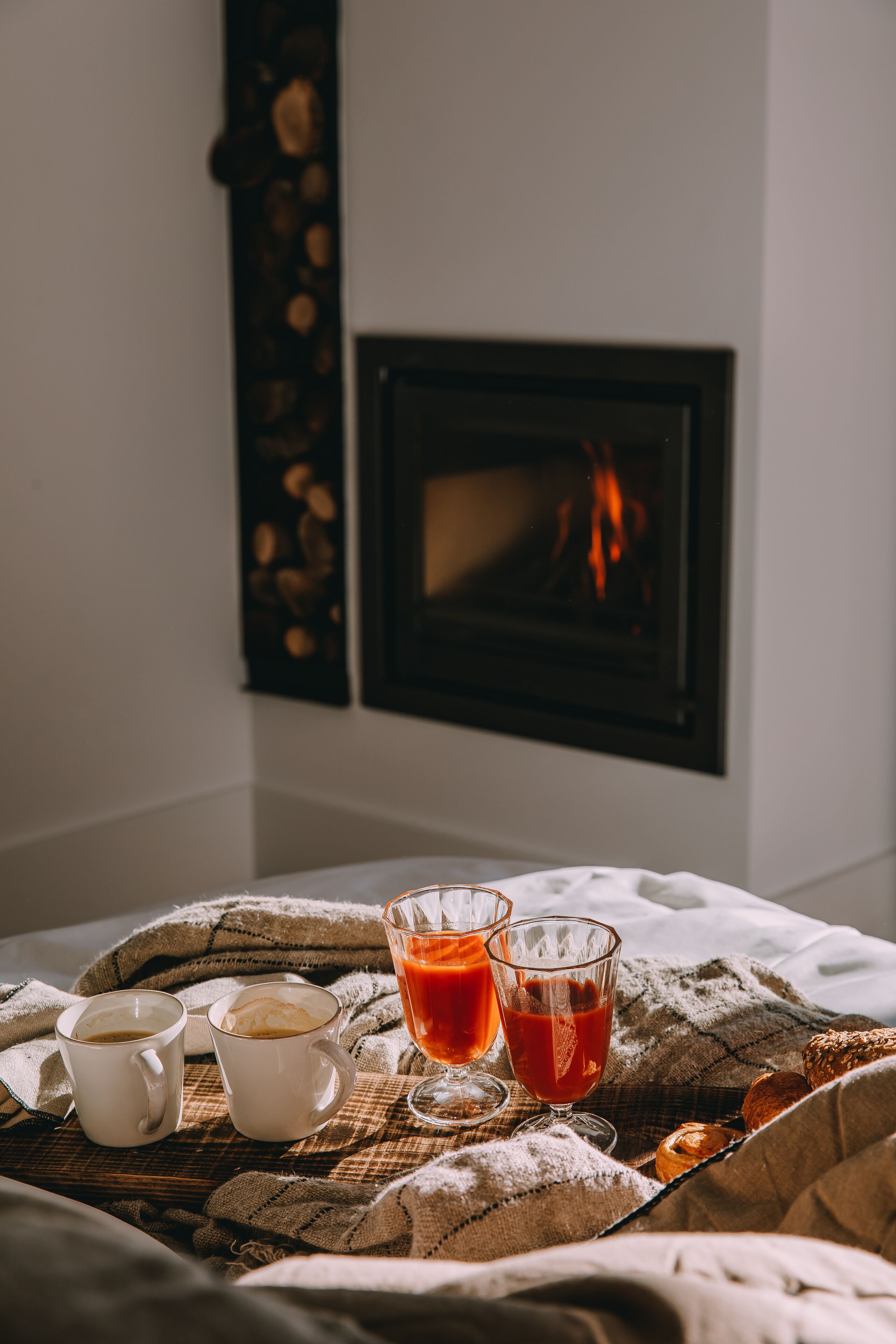 A cozy breakfast setup with two cups of coffee, two glasses of red beverage, and a croissant on a checkered tablecloth.