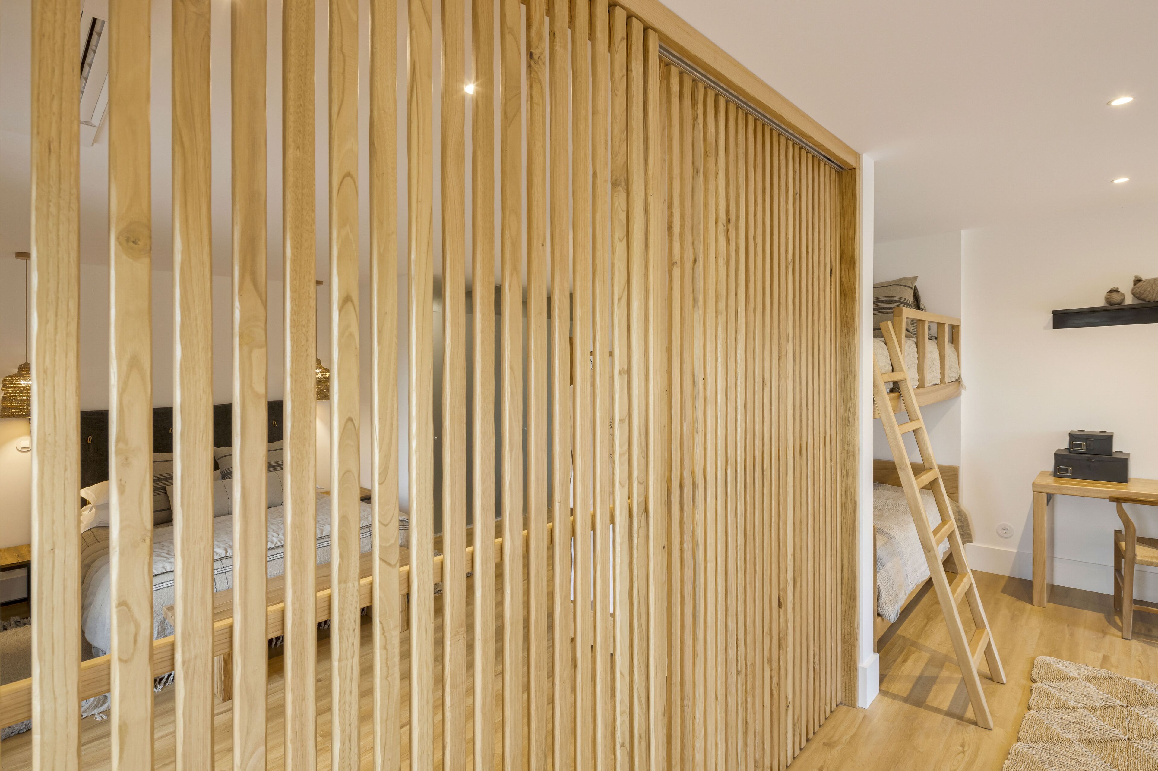A room with a bunk bed, wooden slat partition, and a ladder leading to the upper bunk.