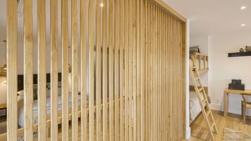 A room with a bunk bed, wooden slat partition, and a ladder leading to the upper bunk.