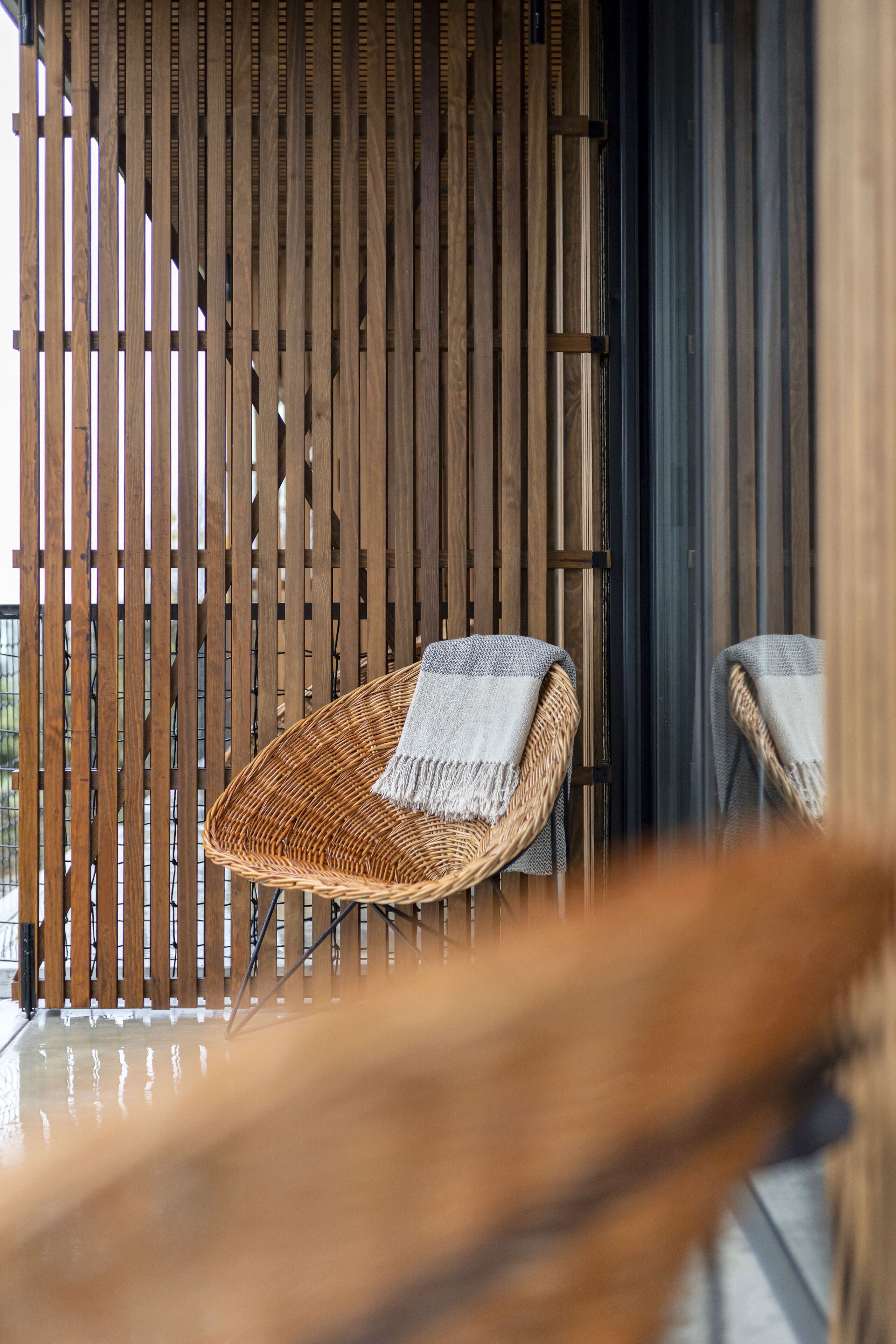 Une chaise en osier, avec une serviette blanche, placée devant un mur en bois à lattes.