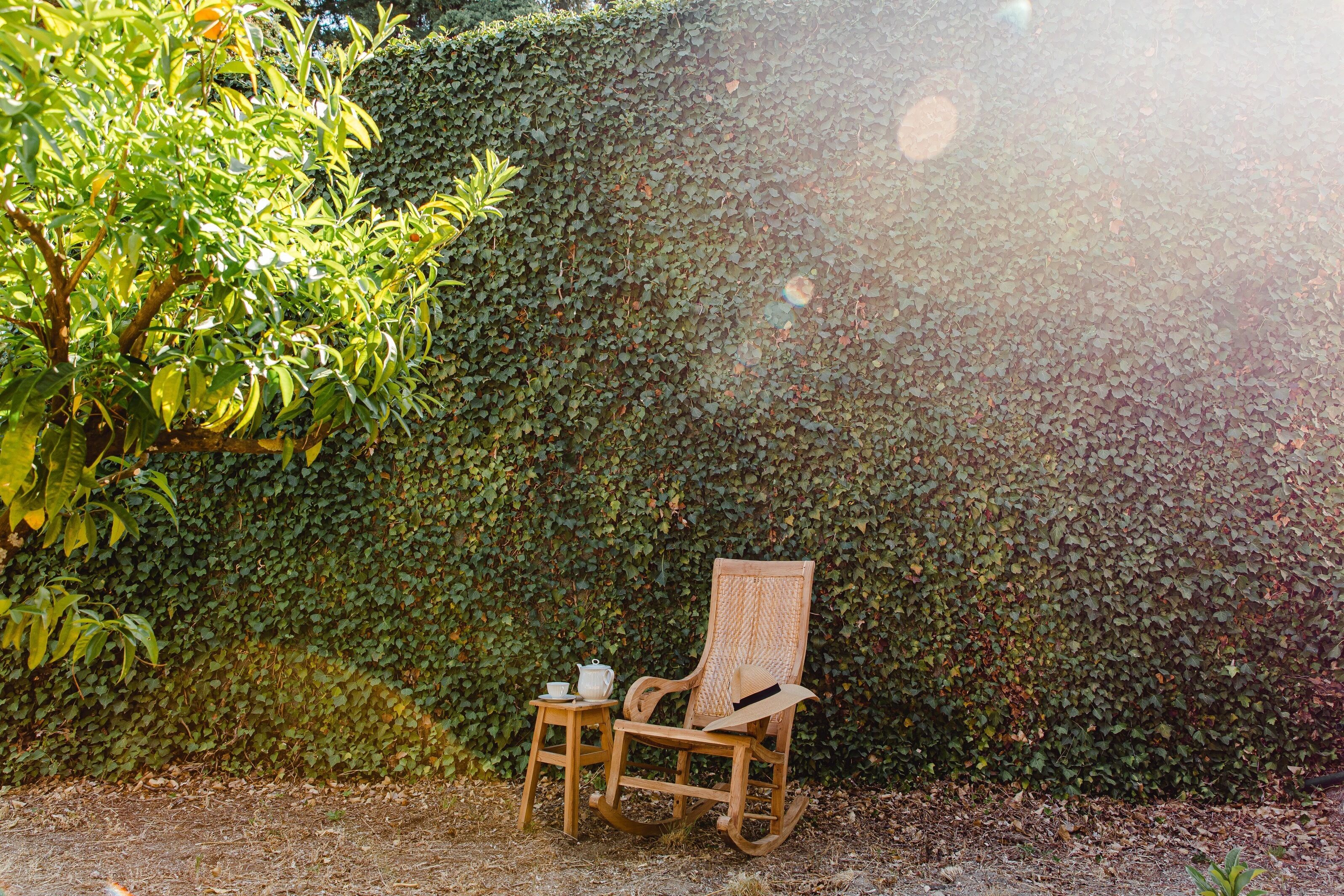 A wooden rocking chair with a woven backrest and a small wooden table beside it, both placed on a gravel surface.