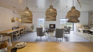 A modern living room with a fireplace, a dining area with a wooden table, and three hanging pendant lights. - TheVagar  (Belmonte)