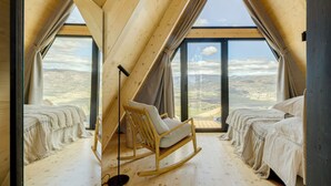 A high-ceilinged room with a wooden interior, two beds, a rocking chair, and large windows offering a view of a mountainous landscape. - TheVagar  (Belmonte)