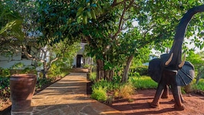 Un sendero conduce a un edificio rodeado de abundante vegetación y una gran estatua de elefante.