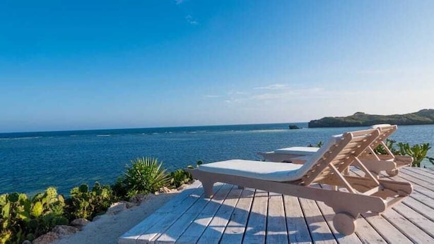 Terraza de madera con dos sillones de relax con vistas al mar azul y despejado.