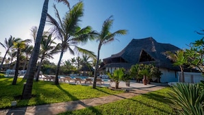 Un resort con una construcción de techo de paja, palmeras y una zona de piscina.
