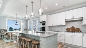 Cocina moderna con armarios blancos, una isla grande con taburetes, electrodomésticos de acero inoxidable e iluminación colgante.