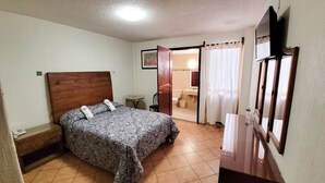 Une chambre à coucher comprenant un lit, une table de chevet, une petite table, une chaise, une salle de bain avec des toilettes et un miroir.
