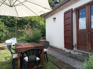 A patio with a wooden table and chairs, a white umbrella, and a brick wall with a wooden door.