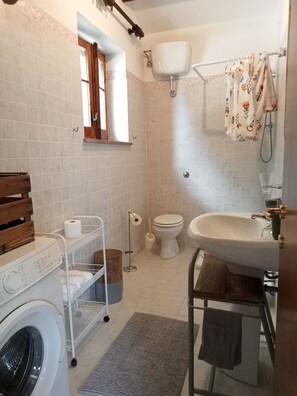 A compact bathroom with a washing machine, toilet, sink, and shower.