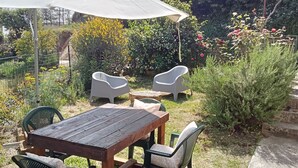 An outdoor patio with a wooden table and chairs, a white umbrella, and a garden with various plants and flowers. - Small cottage near the Sibillini Mountains (Marche)