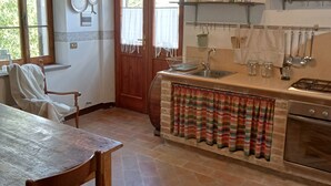 A kitchen with a stone countertop, wooden chairs, a dining table, and a window with curtains. - Small cottage near the Sibillini Mountains (Marche)