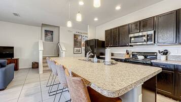 A modern kitchen with a large island, dark cabinets, stainless steel appliances, and pendant lighting.