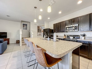 A modern kitchen with a large island, dark cabinets, stainless steel appliances, and pendant lighting. - Themed 4BR Home, Pool, Lazy River, By Disney (Davenport)
