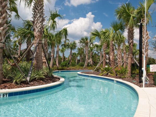 A swimming pool with a curved edge, surrounded by palm trees and a clear blue sky.