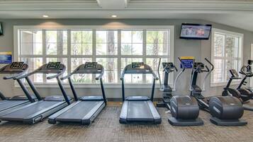 A gym with treadmills, elliptical machines, and a TV screen on the wall.