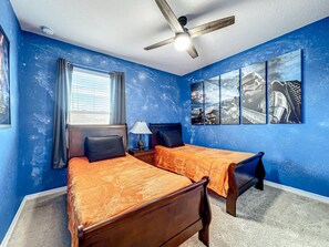 Quarto com duas camas, ventilador de teto e obra de arte na parede.