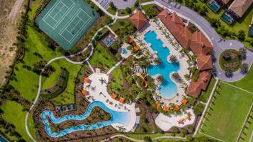 An aerial view of a resort with a large swimming pool, a tennis court, and a winding water feature.